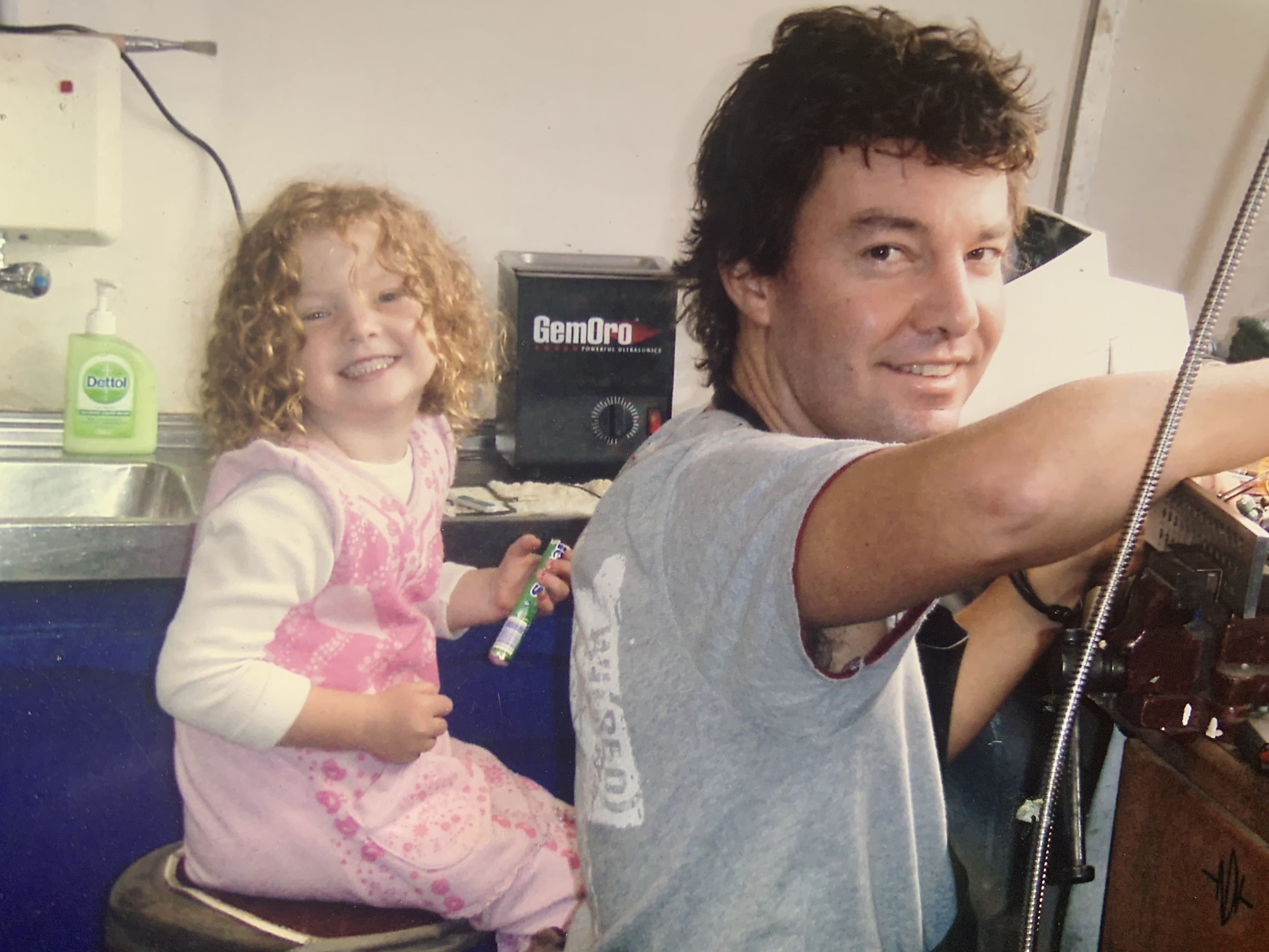 A vintage wooden desk with a mirror in the corner of a room with patterned wallpaper.